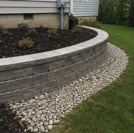 Curved block retaining wall around a planting bed, with a river-rock edge
