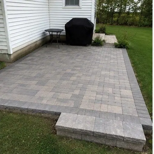 Paver patio off the back of a white house, edged with a border course