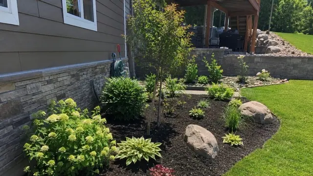 Planting bed with hydrangeas, hostas and boulders beside a house and block retaining wall, by Superior Land Services